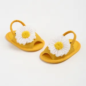 Gros plan détaillé sur des sandales jaunes pour bébé avec une fleur de marguerite blanche.