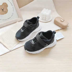 Detailed view of black children's breathable mesh sneakers with Velcro strap on a wooden desk.