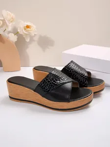 Detalle de sandalias de plataforma negras con tira de cocodrilo y cuña de efecto madera
