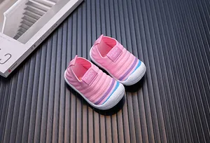 Close-up of pink fly-knit baby walking shoes with rainbow details on dark background.