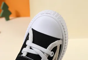 Macro view of the reinforced white rubber toe cap on a black canvas toddler shoe