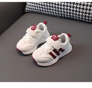 Detailed view of white toddler sneakers with maroon stripes, velcro straps and non-slip sole