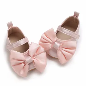 Vista detallada de zapatos de raso rosa para bebé con un gran lazo decorativo elegante y suave