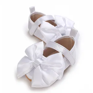 Vista detallada de zapatos de princesa blancos para bebé con gran lazo de raso y suela blanda