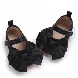 Detalle de zapatos de princesa para bebé en satén negro con lazos grandes y suela blanda.
