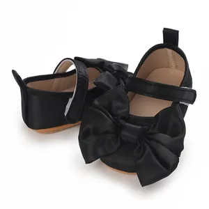 Detalle de zapatos de bebé para niña con un gran lazo de satén negro y suela blanda.