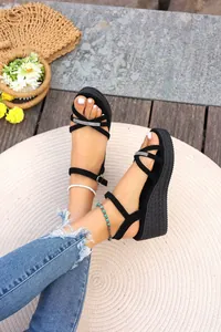 Eleganti sandali neri con zeppa e cinturini incrociati di strass indossati da una modella.
