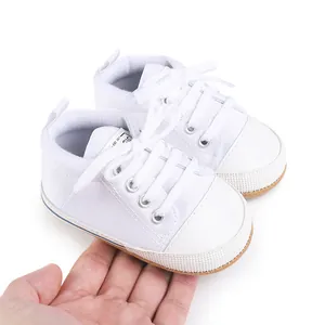 Detail view of classic white newborn canvas walker shoes with durable rubber soles held in hand