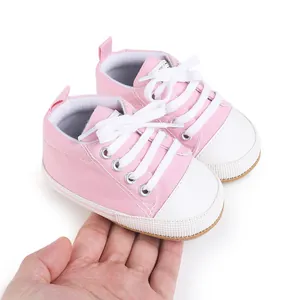 Close-up of pink baby canvas shoes with white rubber sole held in hand for scale