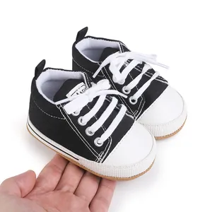 Close-up detail of newborn black canvas baby walker shoes with rubber soles held in hand