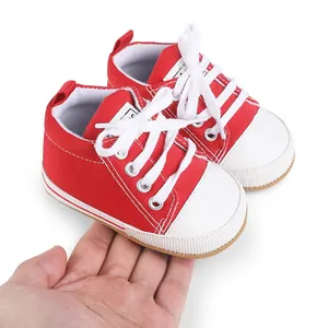 Detailed view of red newborn canvas shoes held in hand to show compact baby size