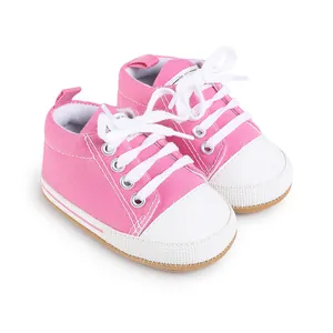 Primer plano de zapatos de lona rosa para bebés con cordones blancos y suelas blandas.