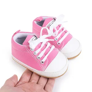 Pink newborn canvas pre-walking shoes held on a hand showing size and soft texture details