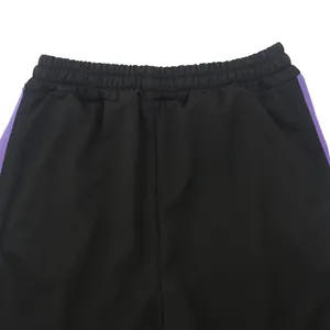 Close-up detail of black slim fit track pants with purple side stripes and elastic waist.