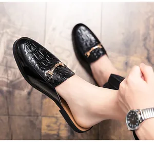 Détail de mules en cuir noir pour hommes avec texture crocodile et boucle dorée.