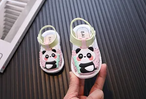 Close-up of pink baby sandal with cute cartoon panda design held by a hand.