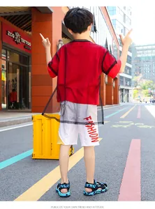 Vista trasera de un niño con sandalias de camuflaje azules y camiseta roja en la calle.