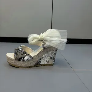 Detalle de sandalia de cuña floral con gran lazo de malla blanca y plataforma.