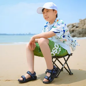Detail view of boy wearing blue patterned beach sandals while sitting on a sandy beach
