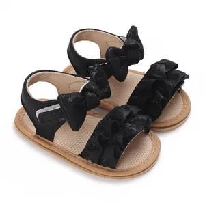 Detailed view of black baby girl sandals featuring ruffles and large bow decorations