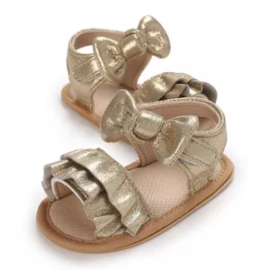 Detailed view of gold shimmering baby sandals with bow and ruffles for summer wear.
