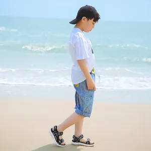 Young boy walking on a sandy beach wearing casual black and white patterned sandals