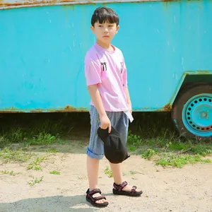 Full view of boy wearing black sport sandals with red stripes in summer outdoor scene