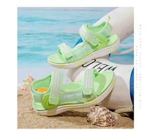 Close-up of light green girls' sandals with heart pattern and soft sole on beach sand