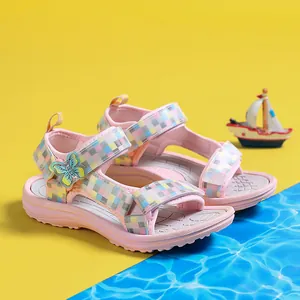 Pink girls' summer sandals with plaid straps and butterfly decor on beach theme background.