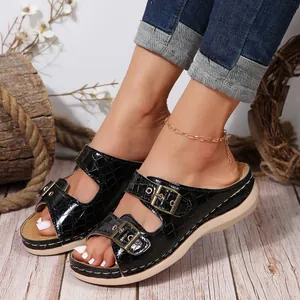 Close-up of black croc-embossed sandals with dual gold buckles and wedge sole.