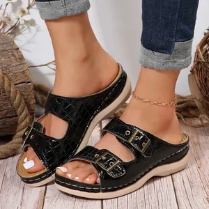 Close-up of black crocodile pattern wedge sandals with ornate gold metal buckles detail