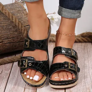 Close-up of black crocodile embossed wedge sandals with double gold-tone metal buckles