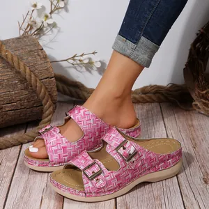 Detail of pink checkered wedge sandals with double metal buckles on a wooden floor.