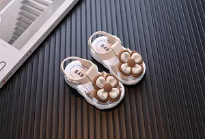 Close-up of beige baby girl sandals with large brown flower décor and closed-toe design.
