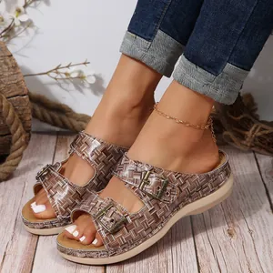 Detail of brown checkered wedge sandals with gold buckles on model's feet.