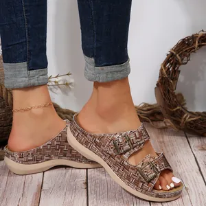 Close-up of women's woven wedge sandals with double metal buckles on wooden floor.