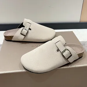 Close-up view of beige suede clogs with adjustable buckle and cork footbed.