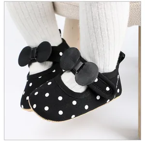 Gros plan de chaussures pour bébé noires à pois avec nœud et semelles souples.