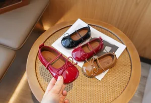 Close-up of glossy girls' bow princess shoes on a rattan table showing elegant details.