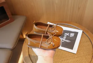 Close-up of caramel patent leather girls' princess shoes featuring a delicate bow