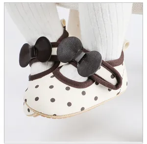 Vue rapprochée de chaussures premier pas bébé fille à pois marrons et nœuds décoratifs.