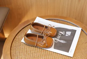 Elegant brown patent leather princess shoes for girls with a decorative bow on a magazine