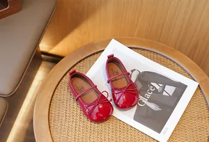 Elegant red patent leather girl's Mary Jane shoes with bow detail placed on a magazine