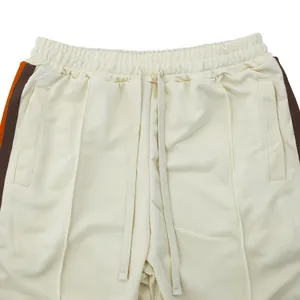 Detailopname van een crème sportbroek met oranje zijstrepen en een handig trekkoordje.