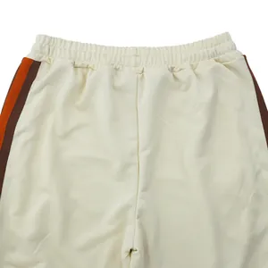 Gedetailleerd overzicht van een crème heren sportbroek met oranje en bruine zijstrepen op taille