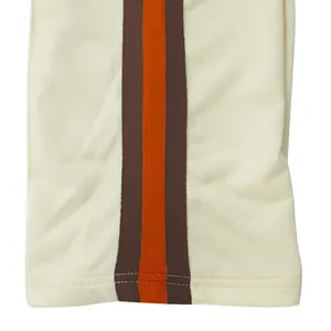 Detailopname van een beige sportbroek met bruine en oranje zijstrepen op de broekspijp
