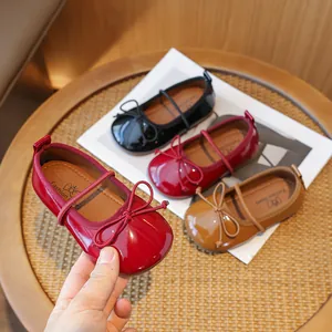 Elegant red girl's Mary Jane shoes with bow tie and soft sole on a wooden table