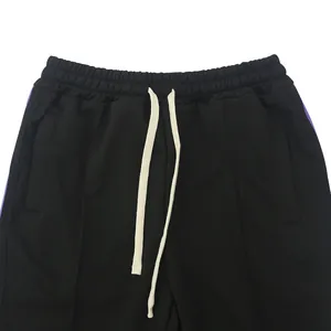 Detail van een zwarte sportbroek met paarse zijstrepen en een trekkoord in de taille
