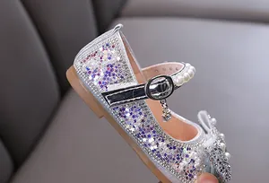 Vista detallada de zapatos de princesa plateados con pedrería brillante y correas de perlas.