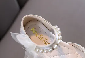 Nahaufnahme eleganter cremefarbener Mädchen-Prinzessinnenschuhe mit Perlen und Schleife